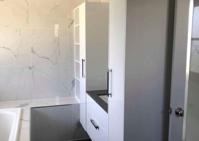 Tall grey storage cabinet beside a vanity in a marble-look tiled bathroom