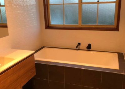 Built-in bath with dark tiled hob and timber vanity under a timber-framed window