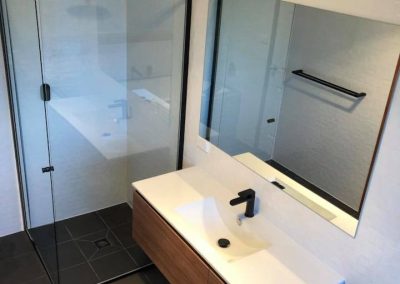 Black-framed shower screen and wall-hung timber vanity with white basin and black mixer