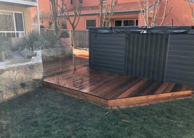 Timber deck platform with a spa in a backyard beside a stone wall