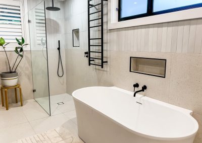 Freestanding bath, walk-in shower and black heated towel ladder in a bright bathroom