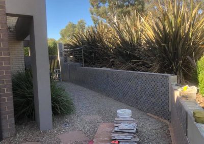Garden retaining wall being clad in patterned tiles, stack of tiles on the path
