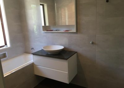 Built-in bath and white wall-hung vanity with dark top and vessel basin
