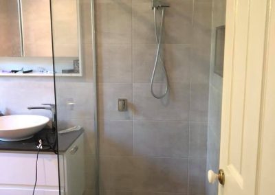 Frameless shower with rail shower beside a white vanity, dark floor tiles