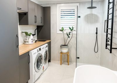 Laundry and bathroom in one, with grey cabinets, timber benchtop and washer and dryer
