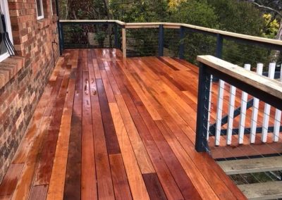 Timber deck along a brick house with a black and timber balustrade