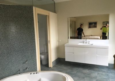 Bathroom with round corner spa bath, green mosaic wall tiles and white vanity