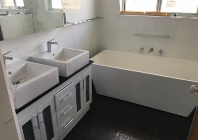 Double vanity with two square basins beside a freestanding bath on dark floor tiles