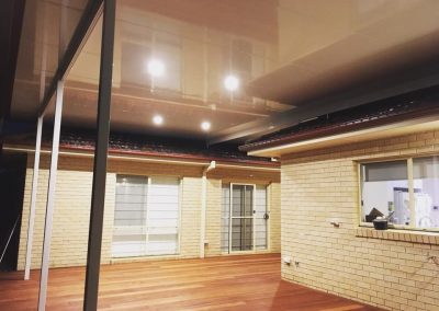 Covered timber deck with downlights in the ceiling beside a brick house