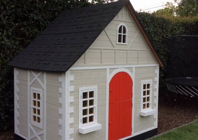 Children's cubby house with a red door on a lawn
