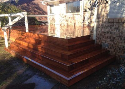 Timber steps wrapping around a raised deck at the back of a brick house