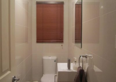 Small bathroom with toilet and wall basin under a timber venetian blind