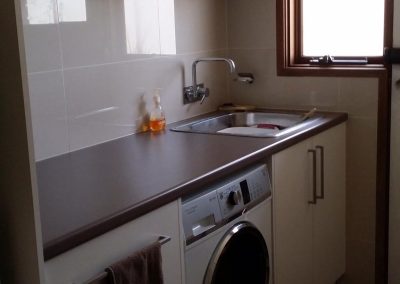 Laundry with dark benchtop, stainless steel sink and washing machine under the bench