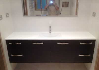 Long wall-hung vanity with dark drawers and white basin top under a wide mirror