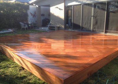 Large freshly oiled timber deck on a lawn behind a house