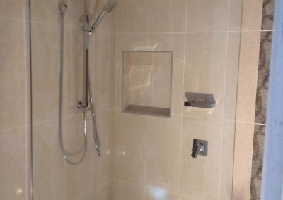 Frameless shower with rail shower, rain head and recessed niche in beige tiles