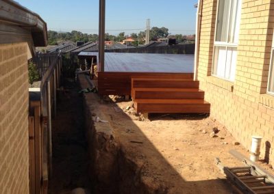 Raised timber deck with a roof and steps beside a house, side yard being excavated