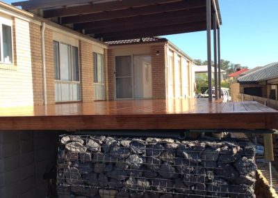 Raised timber deck with a pergola roof on top of a rock-filled gabion wall