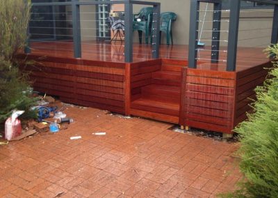 Raised timber deck with steps, glass-roofed pergola and wire balustrade above a paved yard