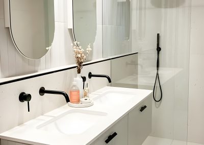 White fluted vanity with oval mirrors beside a walk-in shower