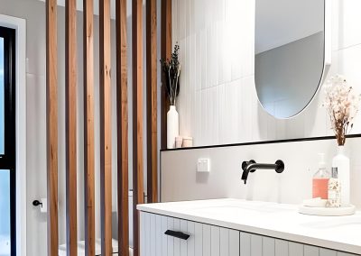 Timber slat divider beside a white fluted vanity, oval mirror and black tapware