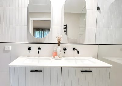 Double vanity with white fluted drawers, two oval mirrors and black tapware