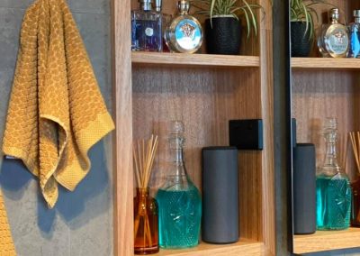 Recessed timber shelf niche in a grey-tiled wall beside a hanging towel