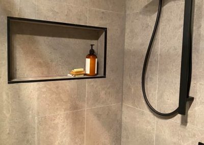 Close view of a recessed shower niche and black rail shower on grey tiles