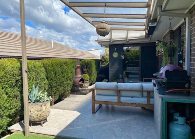 Tiled outdoor area with outdoor lounge and barbecue under a glass-roofed pergola