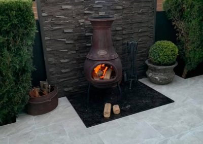 Stacked stone feature wall behind a chiminea on a tiled courtyard