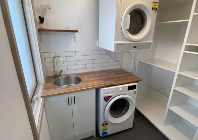 Laundry with stacked dryer, timber benchtop, small sink and open shelving, from the doorway