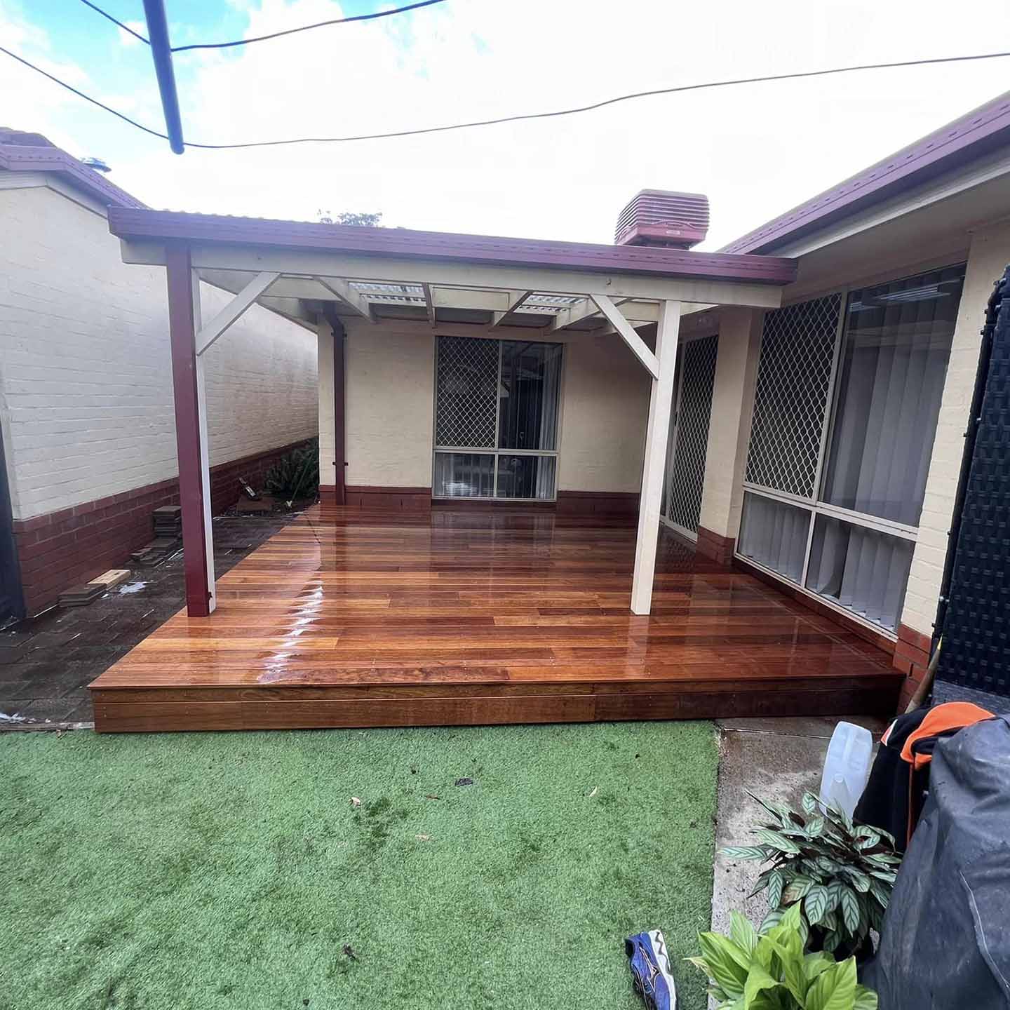 Timber deck under a pergola beside a house, with artificial grass in front