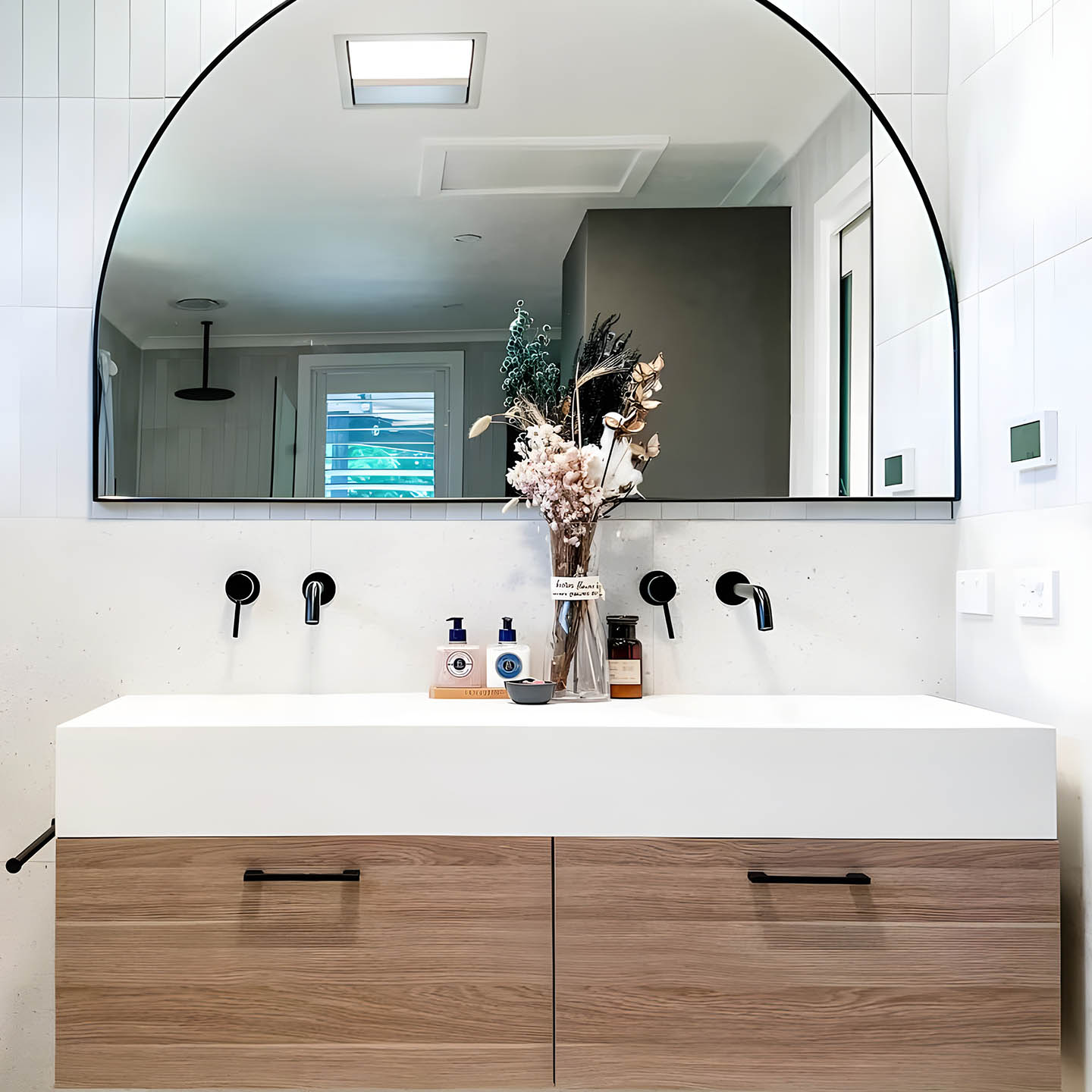 Double white vanity basin with timber drawers, arched mirror and black wall tapware