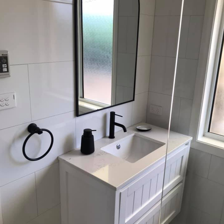 White vanity with black tapware, black towel ring and black-framed mirror