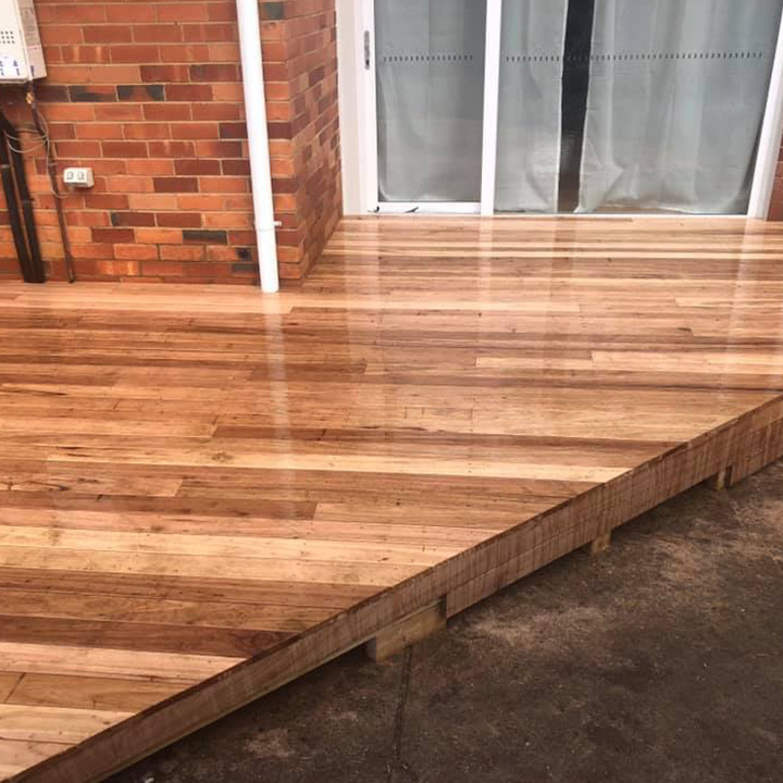 Freshly oiled timber deck with a raised edge beside a brick wall