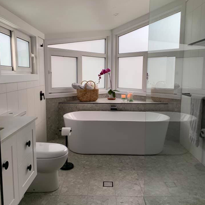 Freestanding bath beneath frosted corner windows in a bright white bathroom