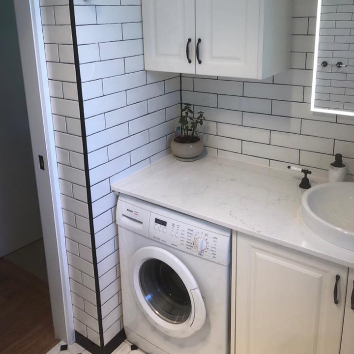 Laundry with white subway tiles, washing machine under the bench and round basin