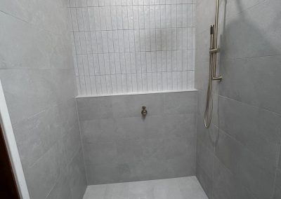 Walk-in shower with brass rain shower head and white vertical feature tiles