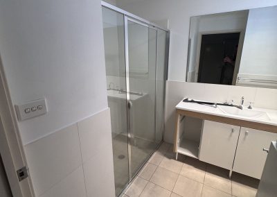 Bathroom with beige floor tiles, framed glass shower and white vanity