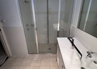 Framed glass shower and white vanity with a black towel rail