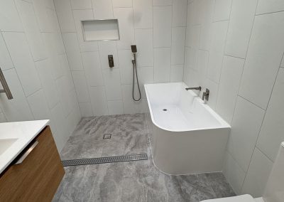 Bathroom with a bath inside an open shower area, timber vanity and grey floor tiles