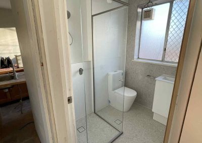 Bathroom with framed glass shower, toilet and white vanity, seen from the doorway