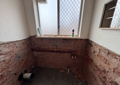 Stripped bathroom with exposed brick walls and new floor screed under the window