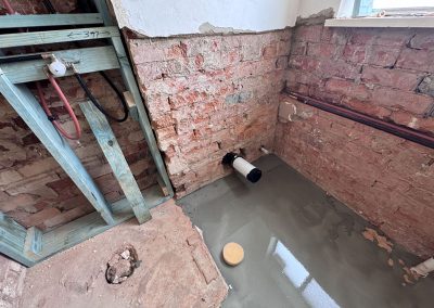 In-wall frame and new pipework against exposed brickwork beside fresh floor screed