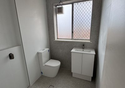 Finished bathroom with toilet, white vanity, white wall tiles and speckled floor tiles
