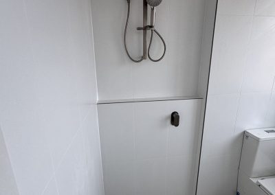 Shower with brushed rail shower, white wall tiles and speckled floor tiles