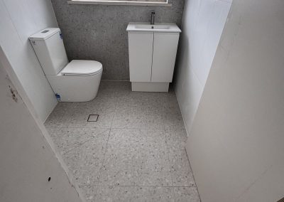 Small bathroom with toilet, compact white vanity and speckled floor tiles