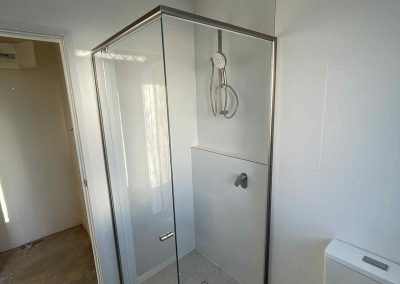 Corner shower with framed glass screen and white wall tiles