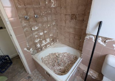 Old pink-tiled bathroom with the bath full of rubble during demolition