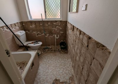 Bathroom part-way through demolition, tiles stripped from the walls and floor